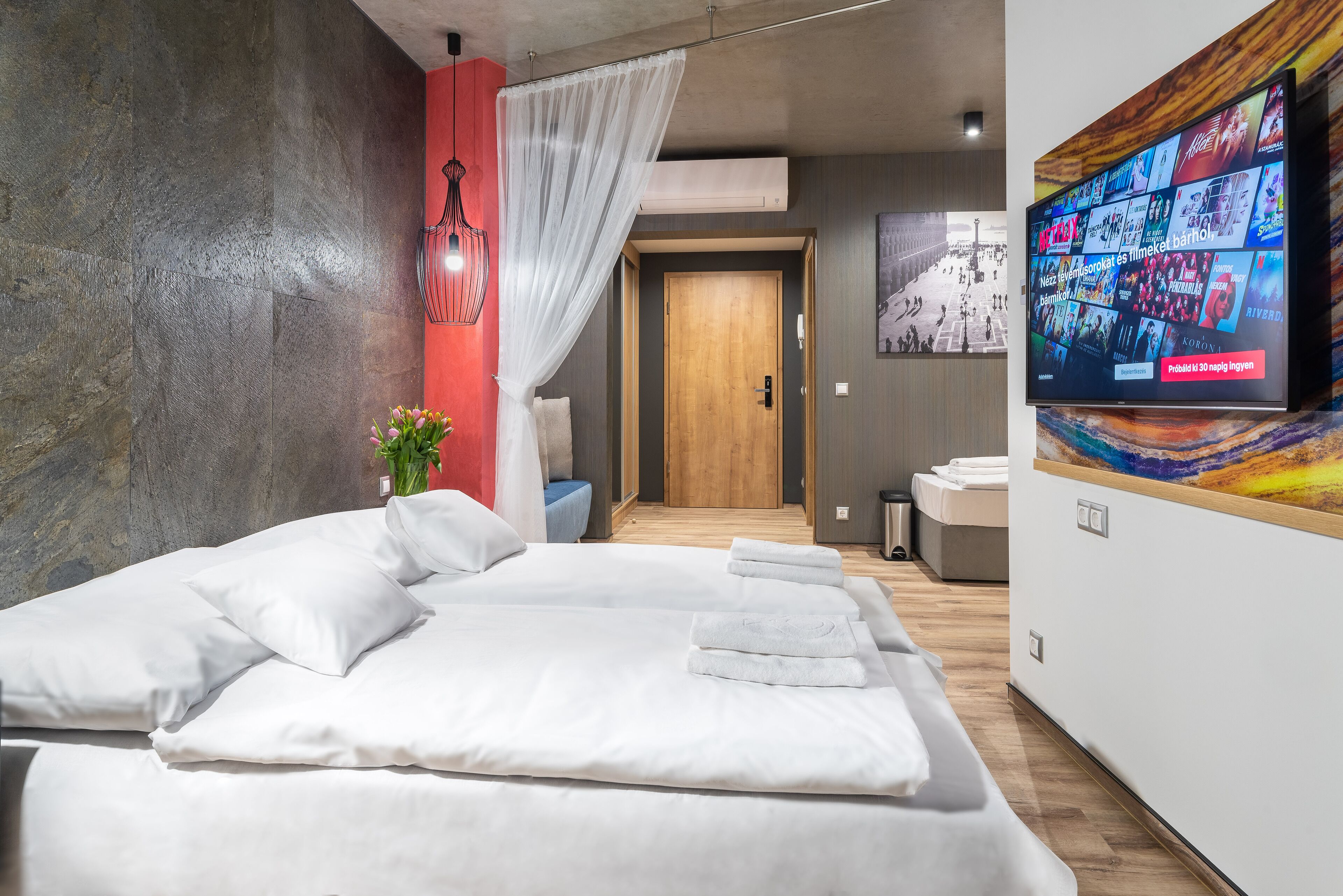 A modern hotel room with a large bed, a TV displaying various channels, and a wooden door in the background.