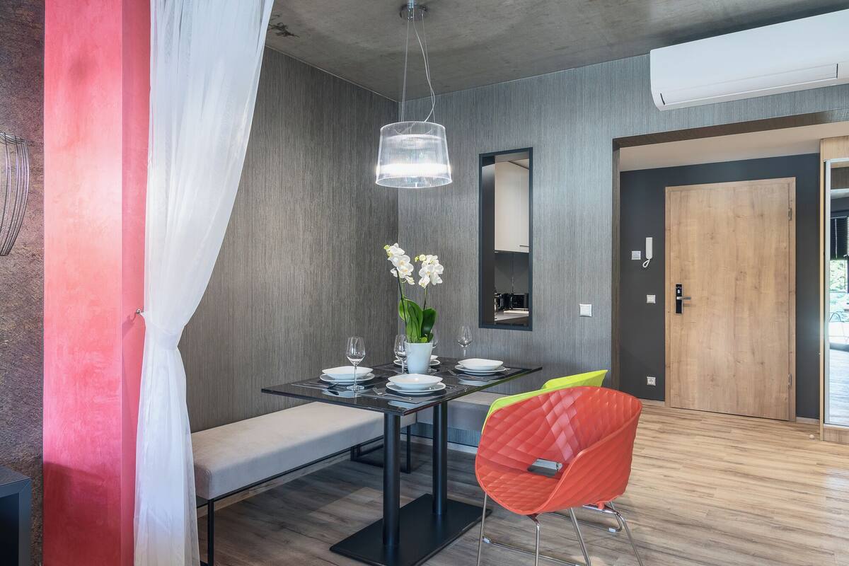 A modern dining area with a glass table, white chairs, a bench, and a vibrant red chair.