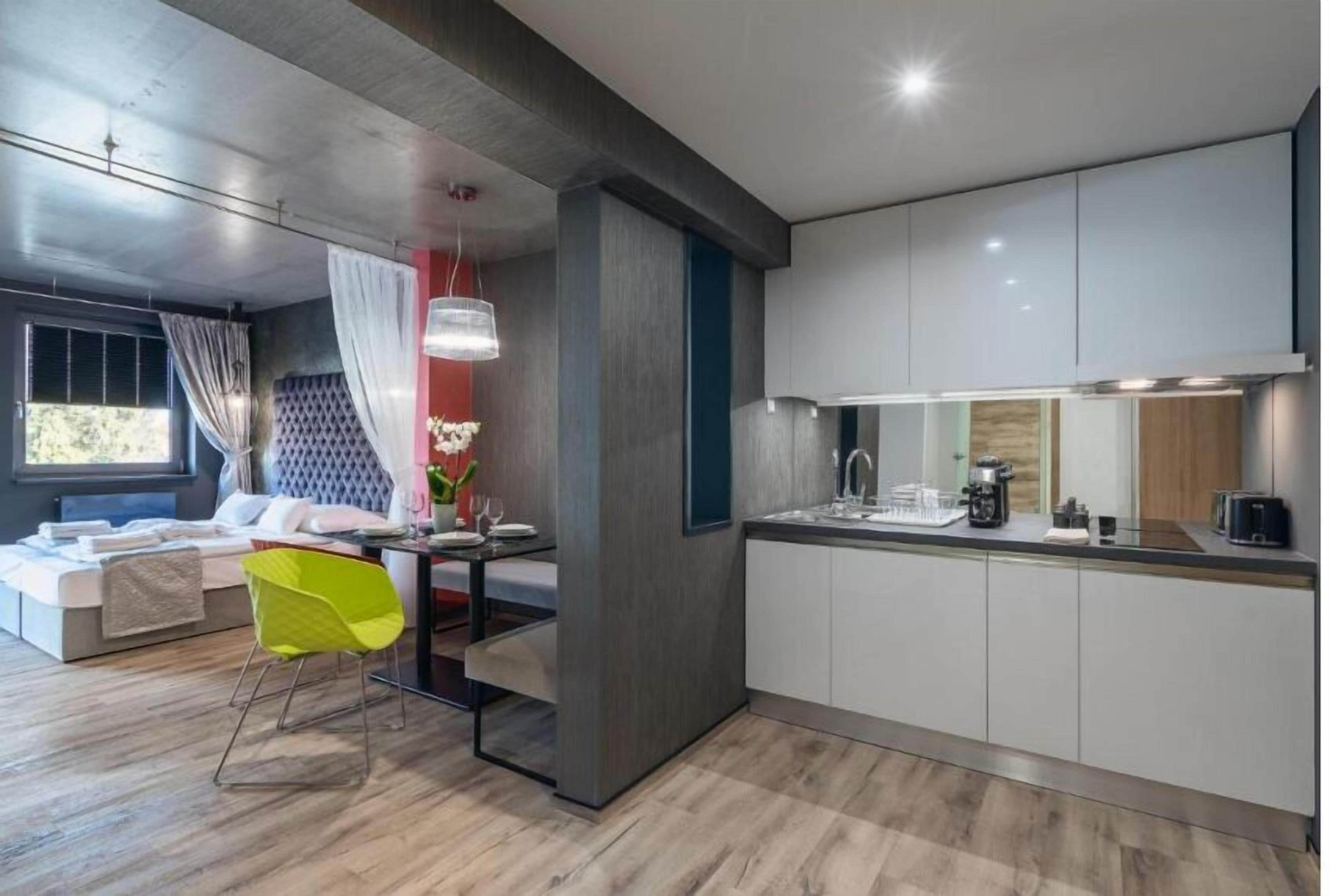 Una cocina moderna con armarios blancos, un comedor con una silla de color amarillo brillante y un ventanal con cortinas.