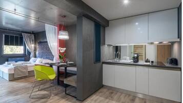 A modern kitchen with white cabinets, a dining area with a bright yellow chair, and a large window with curtains.