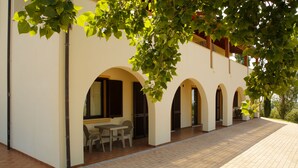 A building with a covered outdoor area featuring a table and chairs, arched doorways, and a tiled floor. - Agriturismo San Gregorio (San Vincenzo)