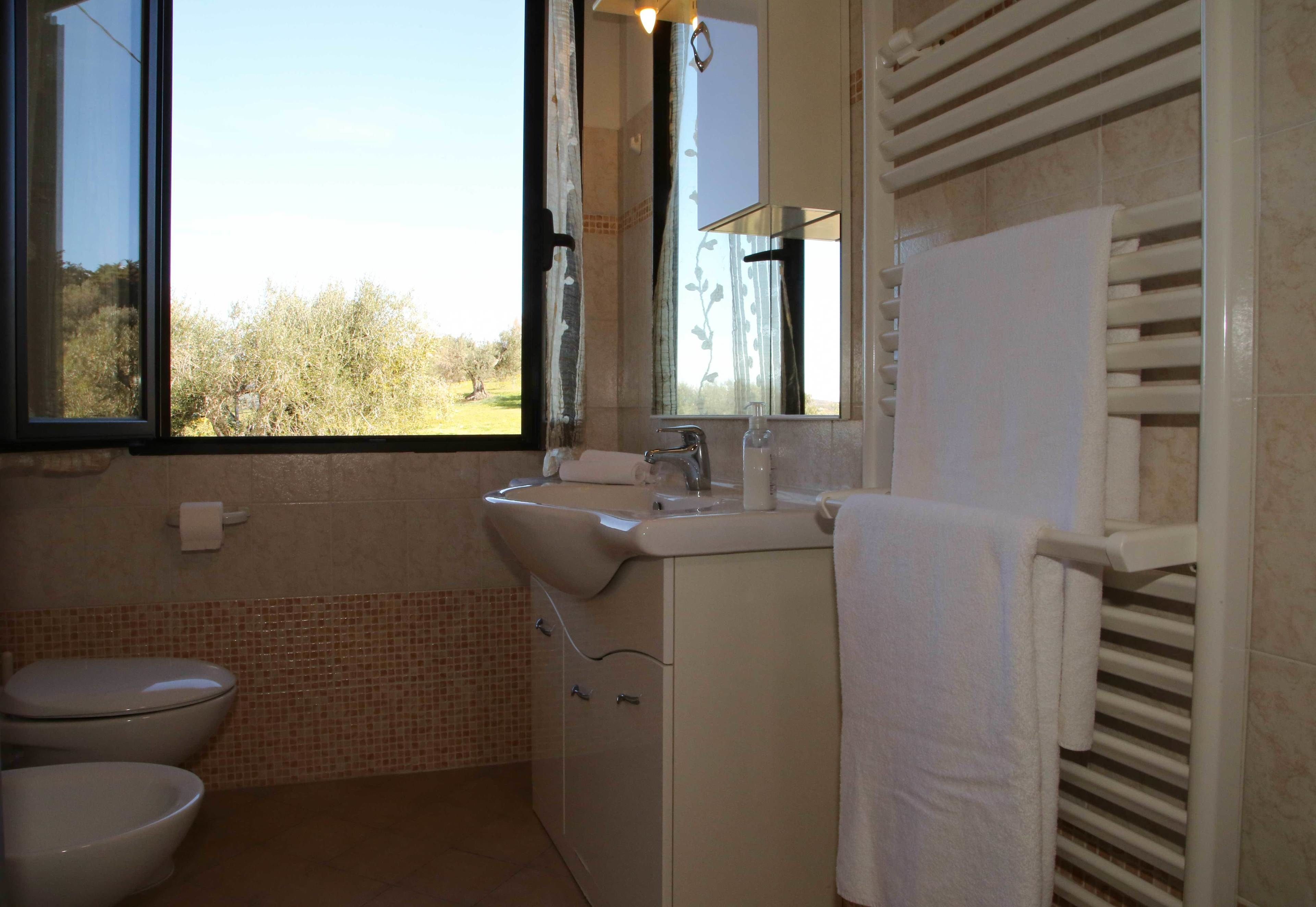 Une salle de bain équipée de toilettes, d’un lavabo et d’une fenêtre donnant sur la verdure.
