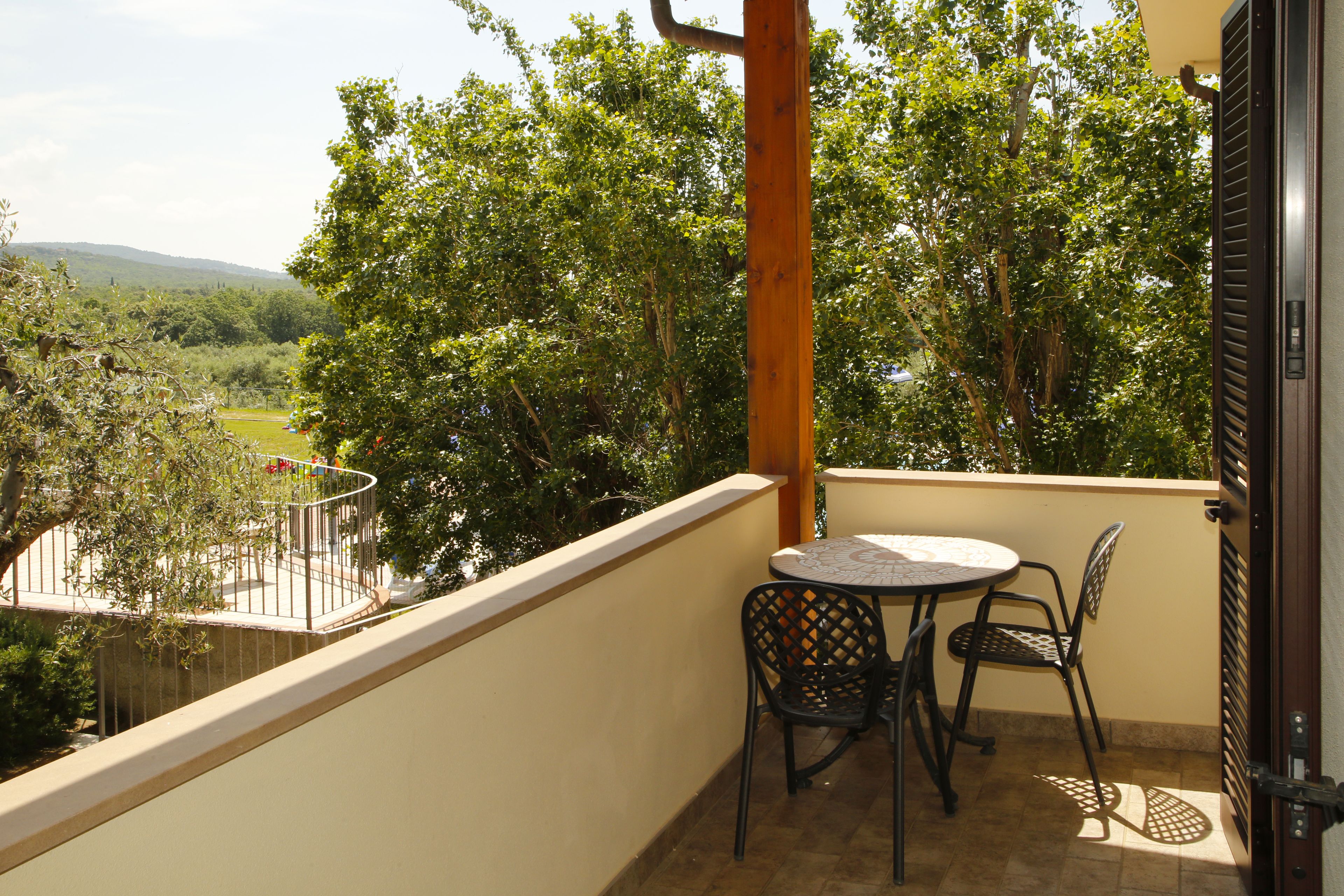 Ein Balkon mit Tisch und Stühlen, mit Blick auf einen Garten und Bäume.