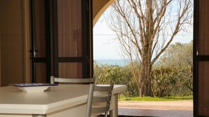 A dining area with a table and chairs, a view of the outdoors including trees and a body of water. - Agriturismo San Gregorio (San Vincenzo)