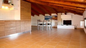 A modern kitchen with wooden cabinets, a dining area with chairs, a TV, and a painting on the wall. - Agriturismo San Gregorio (San Vincenzo)