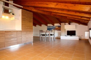 Una cocina moderna con armarios de madera, un comedor con sillas, un televisor y un cuadro en la pared.