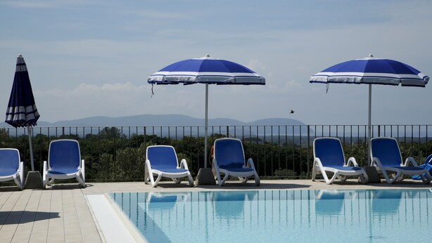 A poolside area with lounge chairs and umbrellas, a clear sky, and mountains in the background. - Agriturismo San Gregorio (San Vincenzo)