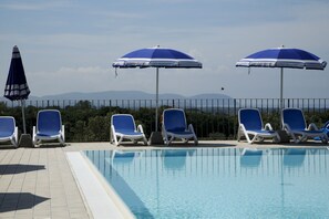 A poolside area with lounge chairs and umbrellas, a clear sky, and mountains in the background. - Agriturismo San Gregorio (San Vincenzo)