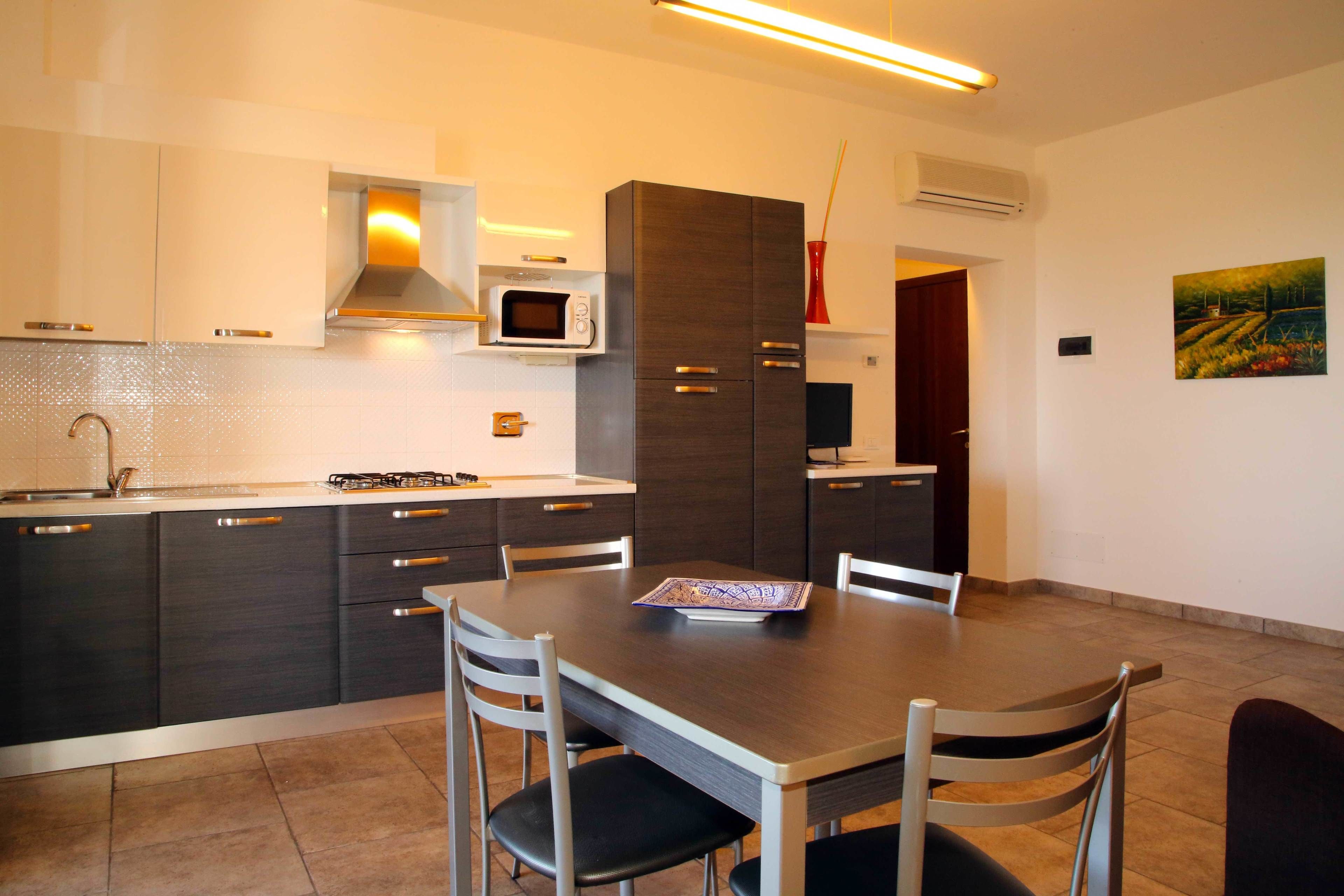 A modern kitchen with dark cabinetry, a microwave, and a dining table with chairs.
