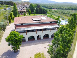 Un edificio de dos pisos con techo de tejas, ventanas arqueadas y un patio con mesas al aire libre.