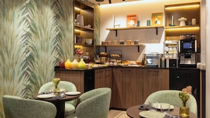 Una cocina moderna con armarios de madera, una cafetera y un comedor con sillas tapizadas de verde y una mesa redonda.