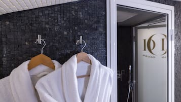 A bathroom with two white towels hanging on wooden hangers, a glass door with a logo, and a shower area with a handheld showerhead.