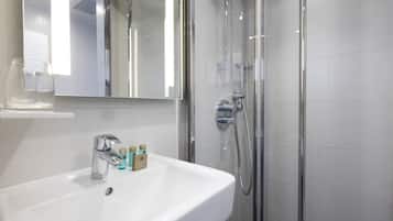 A modern bathroom with a white sink, a mirror, and a glass-enclosed shower.