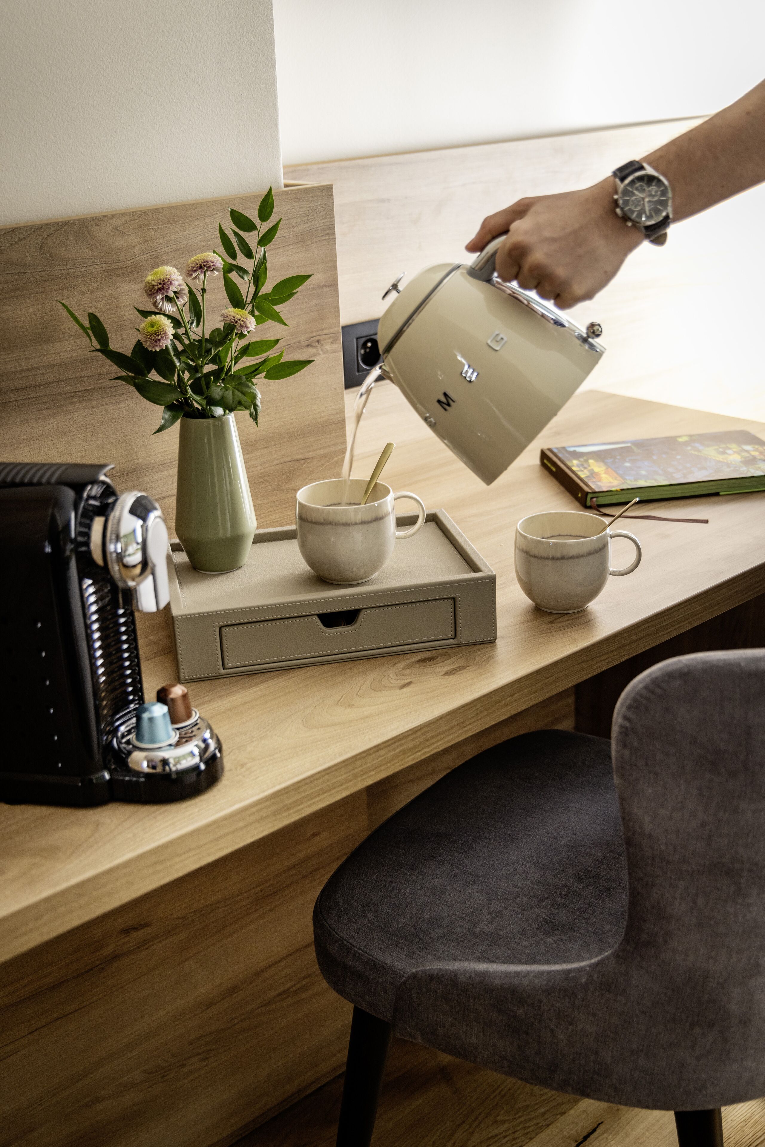 Een houten bureau met een koffiezetapparaat, een mok, een dienblad en een boek.