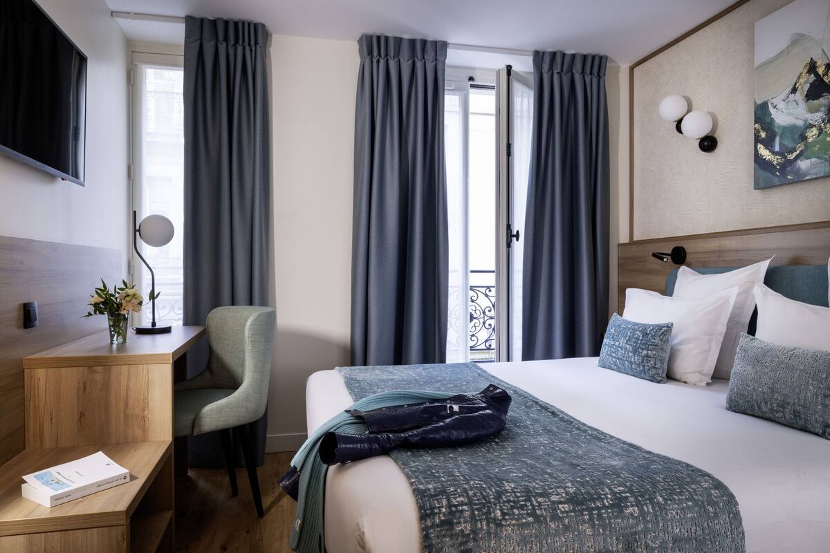 Une chambre d’hôtel avec un lit, un bureau, une chaise, une télévision et un tableau au mur.
