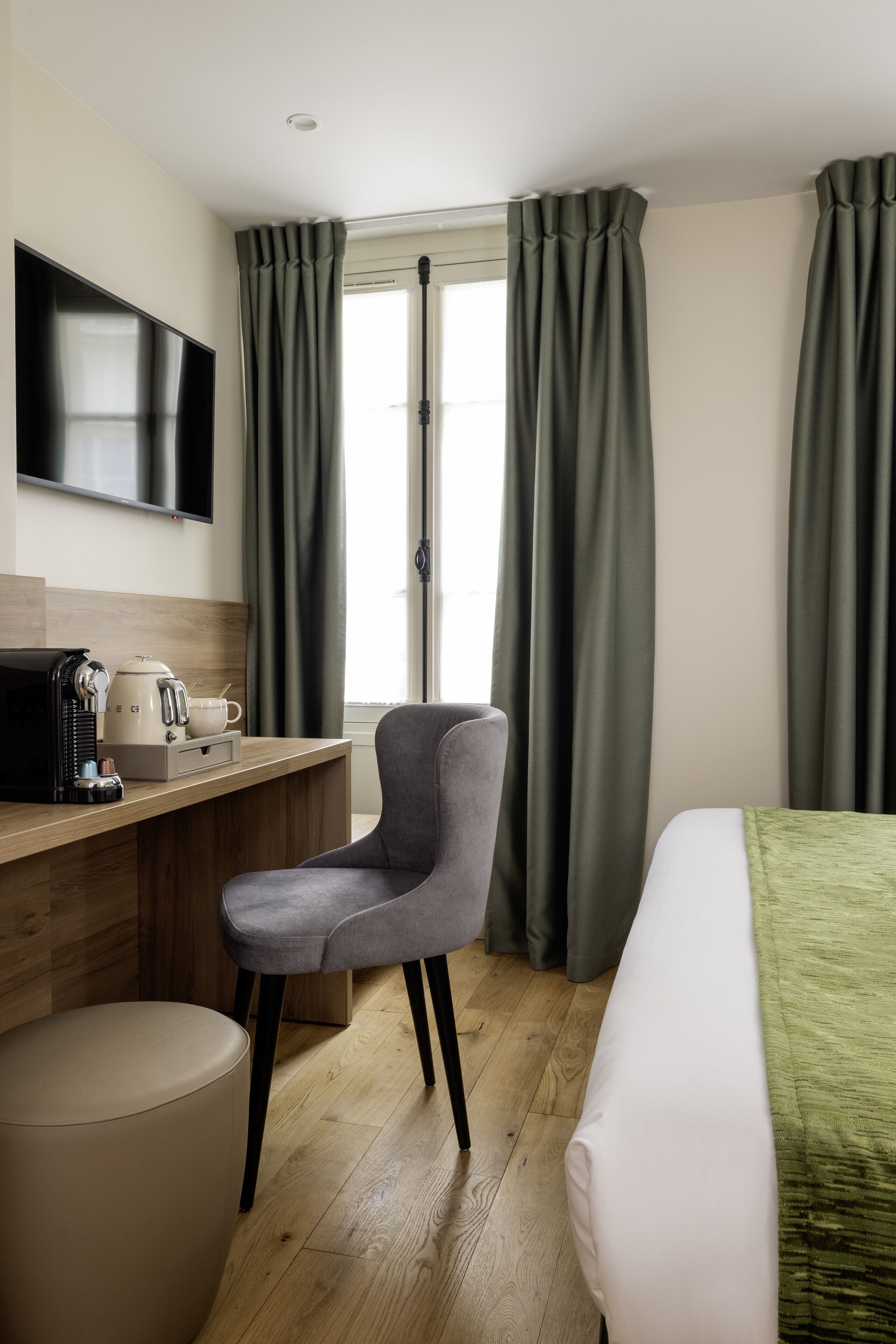 Una habitación de hotel con cama, escritorio y silla, televisor, cafetera y cortinas.