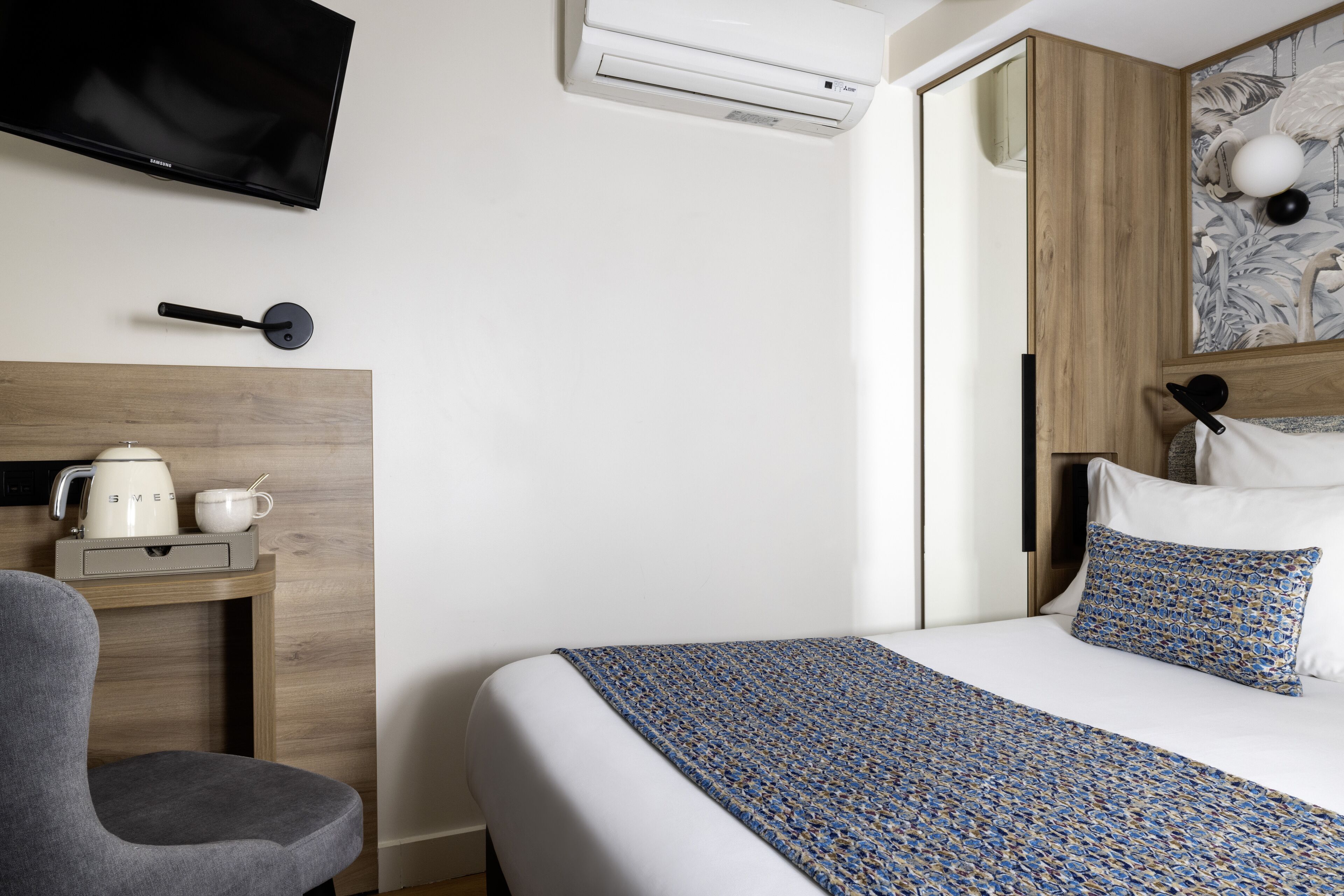 A hotel room with a bed, a TV mounted on the wall, a coffee maker, and a wooden headboard.
