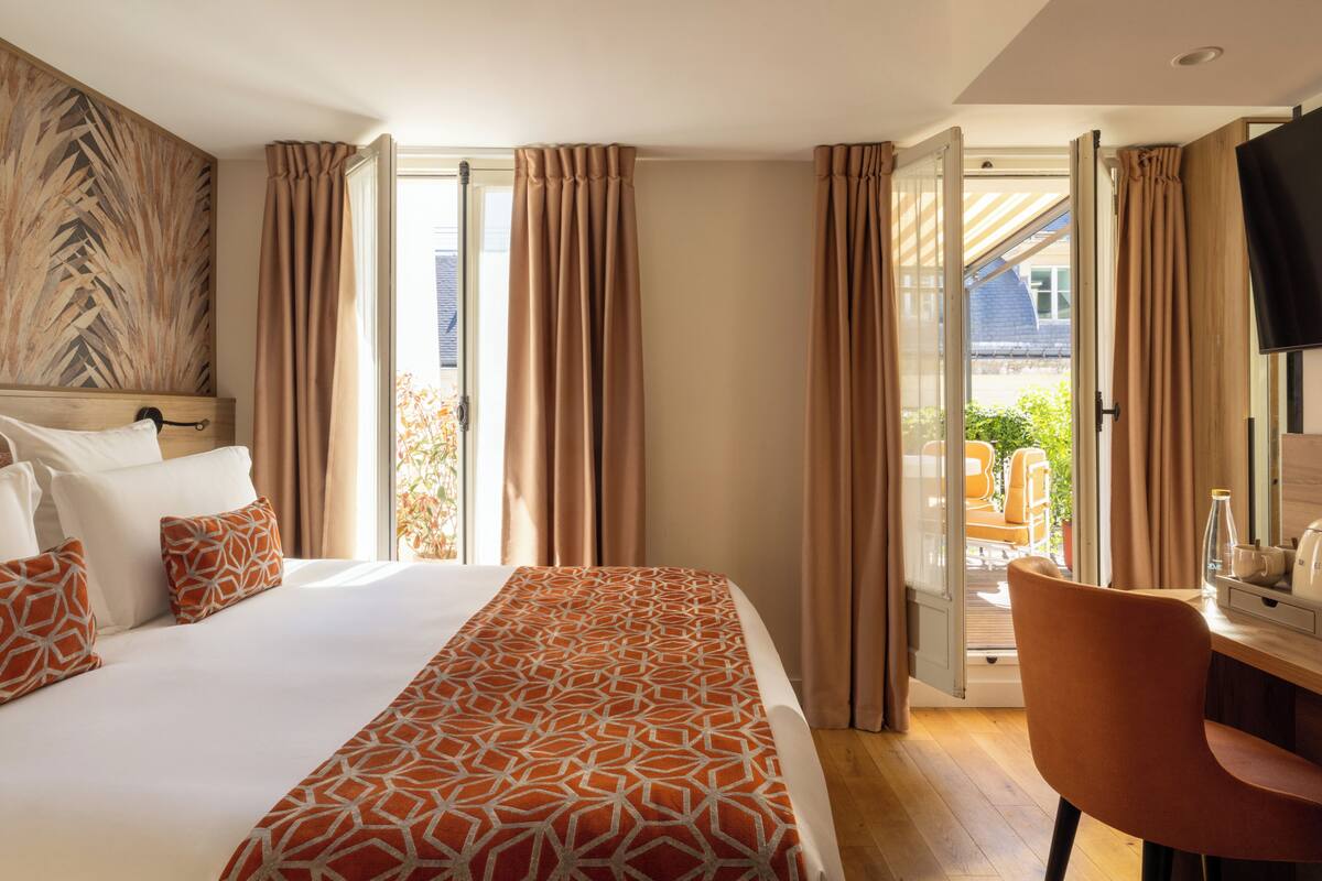 Quarto de hotel com uma cama, uma escrivaninha, uma cadeira e uma televisão.