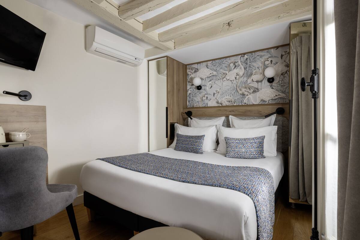 Quarto com cama, poltrona, televisão e ar-condicionado fixado na parede.