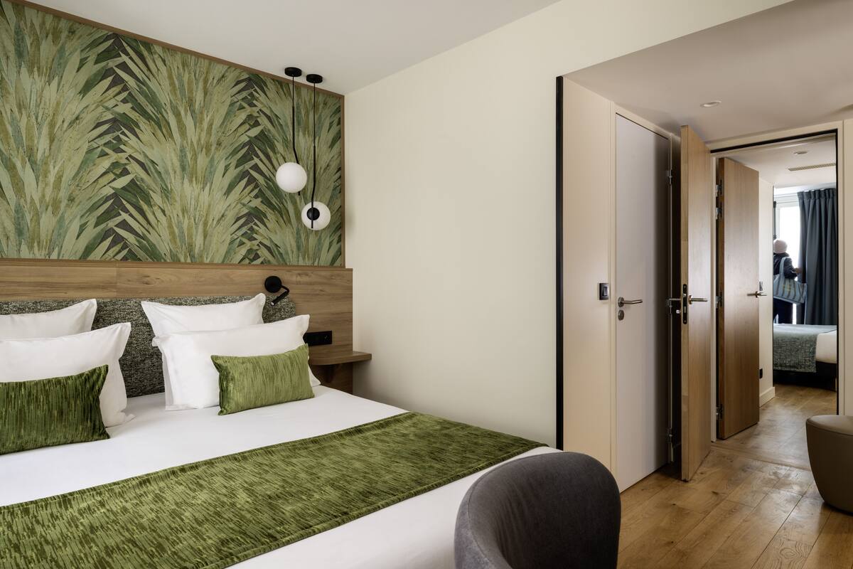 Quarto de hotel moderno com uma cama grande, cabeceira de madeira e parede com padrão de folhas verdes.