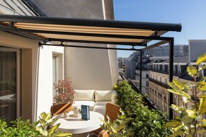 A balcony with a table, chairs, a sofa, and a potted plant.