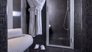 Un baño moderno con mampara de vidrio, una alfombra de baño blanca y una bata blanca colgada en la pared.