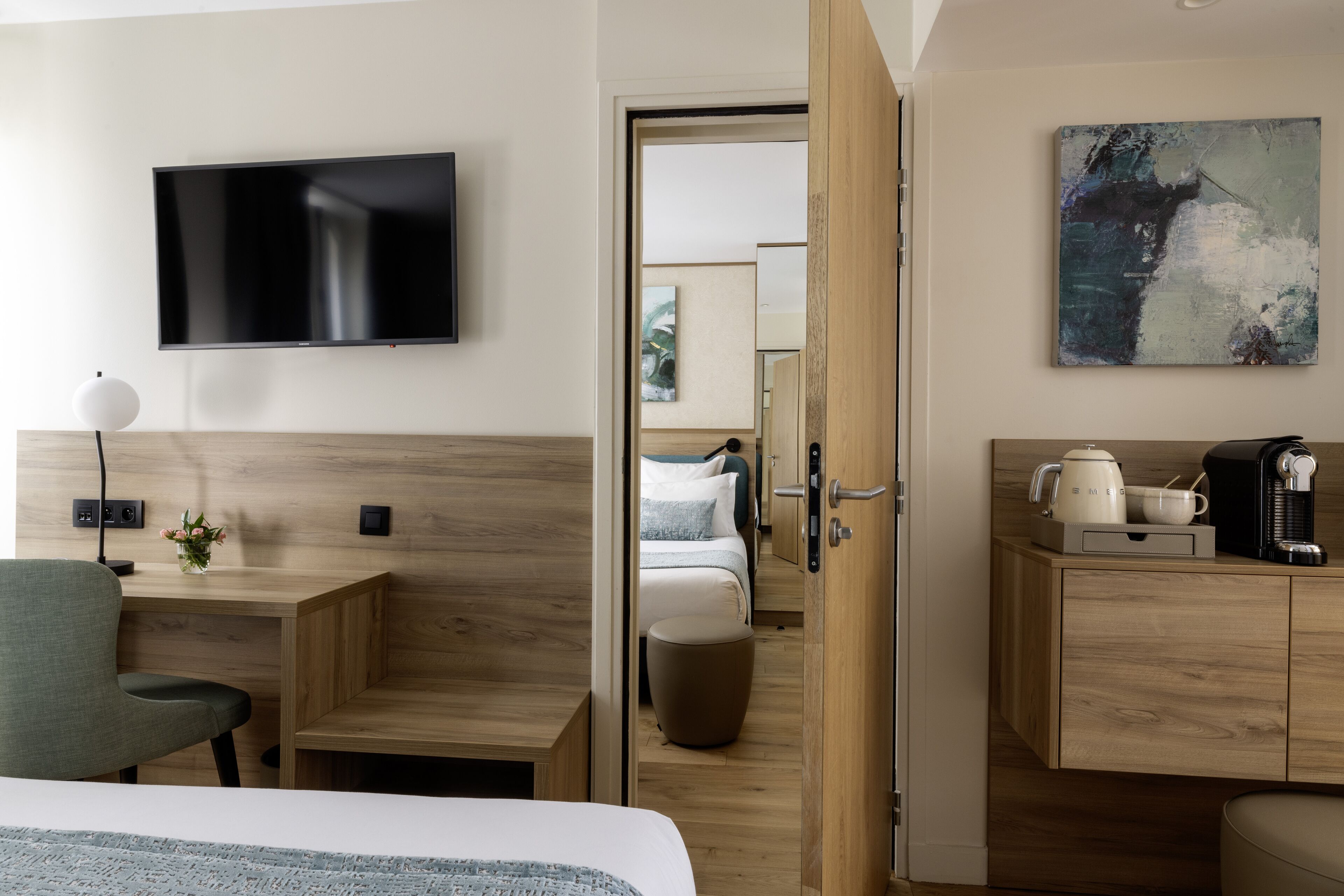 A hotel room with a bed, a desk, a chair, a TV, a coffee maker, and a painting on the wall.