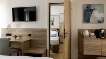 A hotel room with a bed, a desk, a chair, a TV, a coffee maker, and a painting on the wall.
