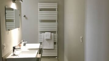 A narrow bathroom with two sinks, a mirror, and a towel rack.
