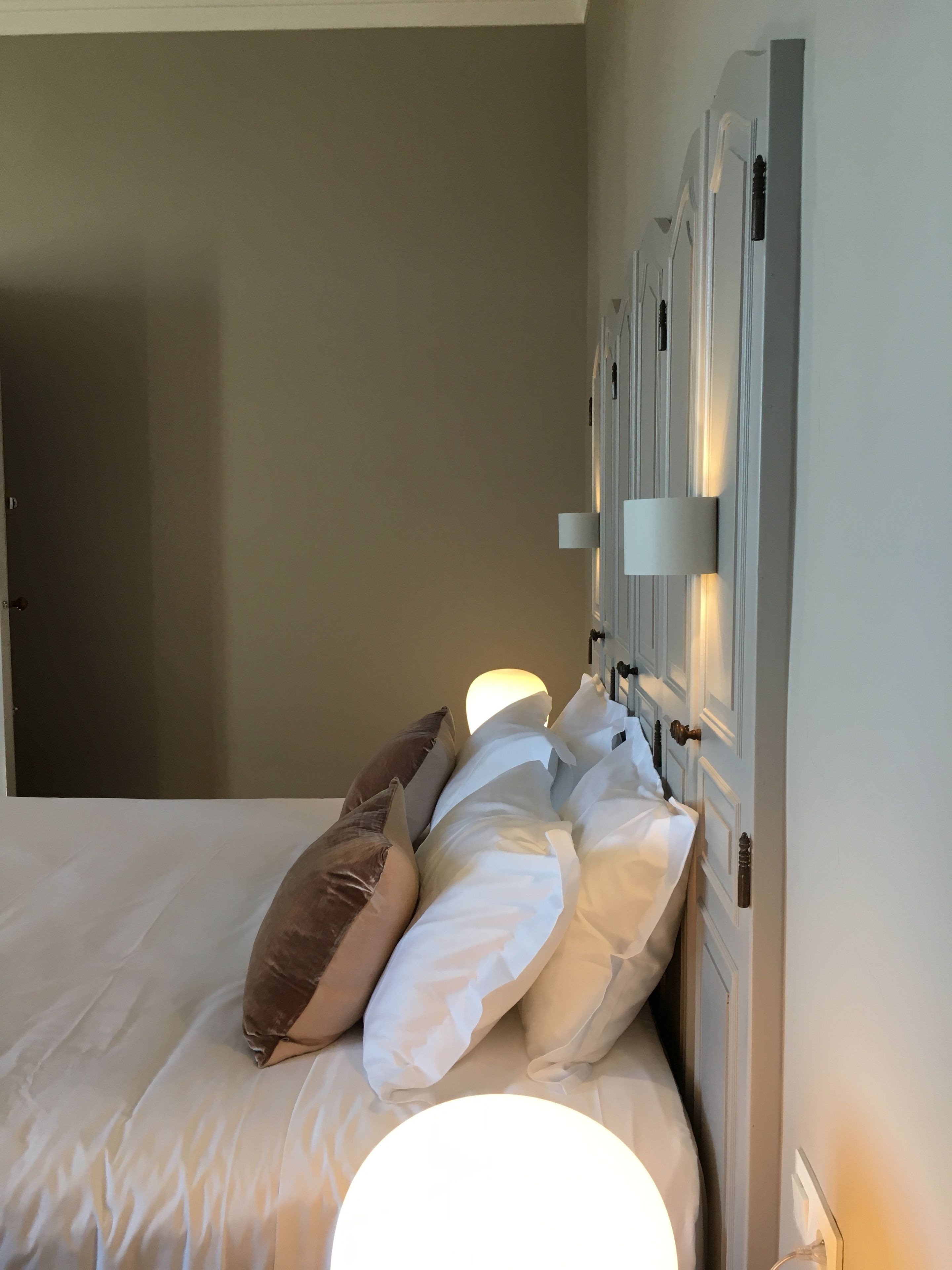 A neatly made bed with white and brown pillows, a bedside lamp, and a door with a light switch.