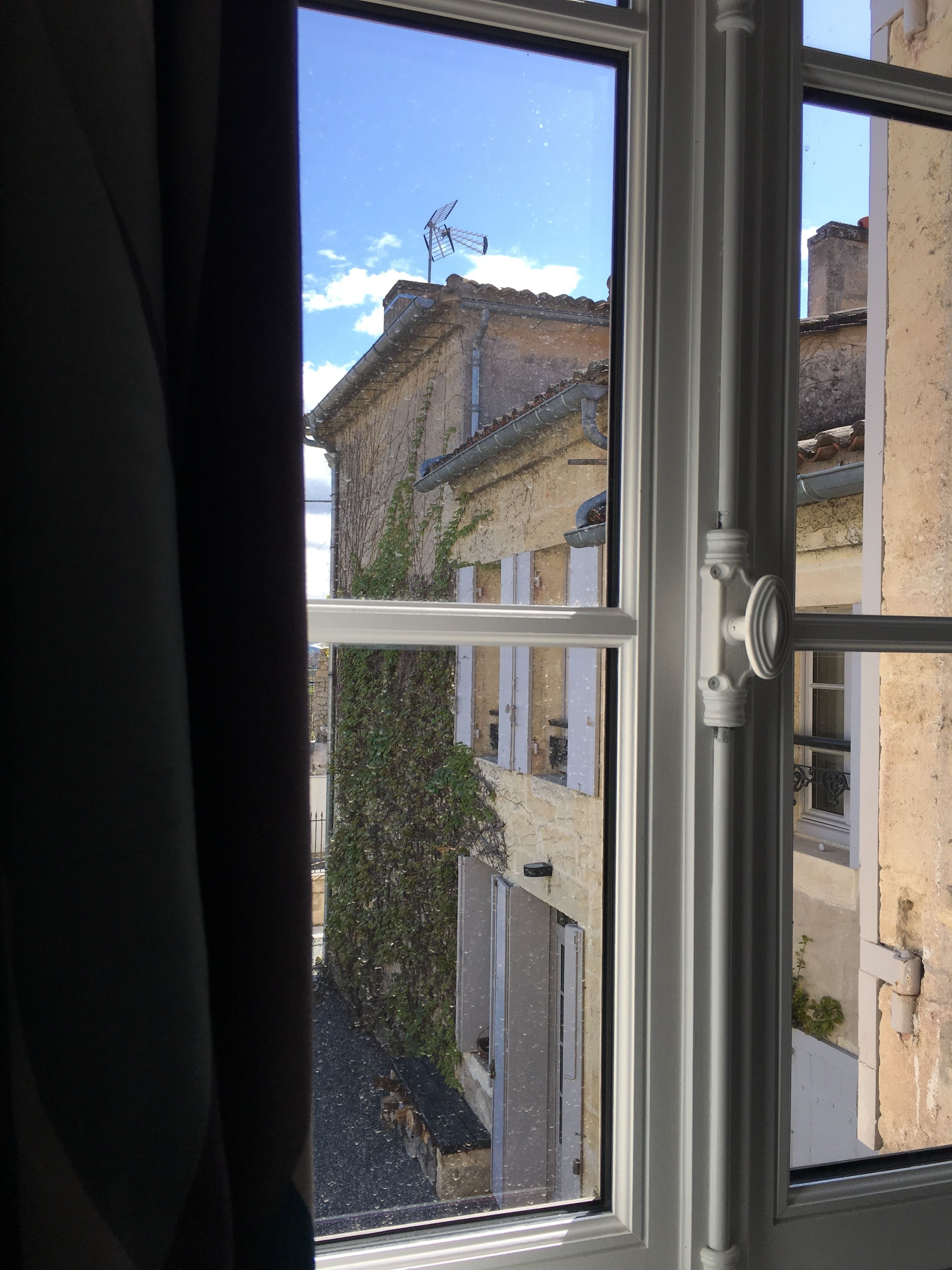 A window with a view of a building with a weather vane and a balcony.