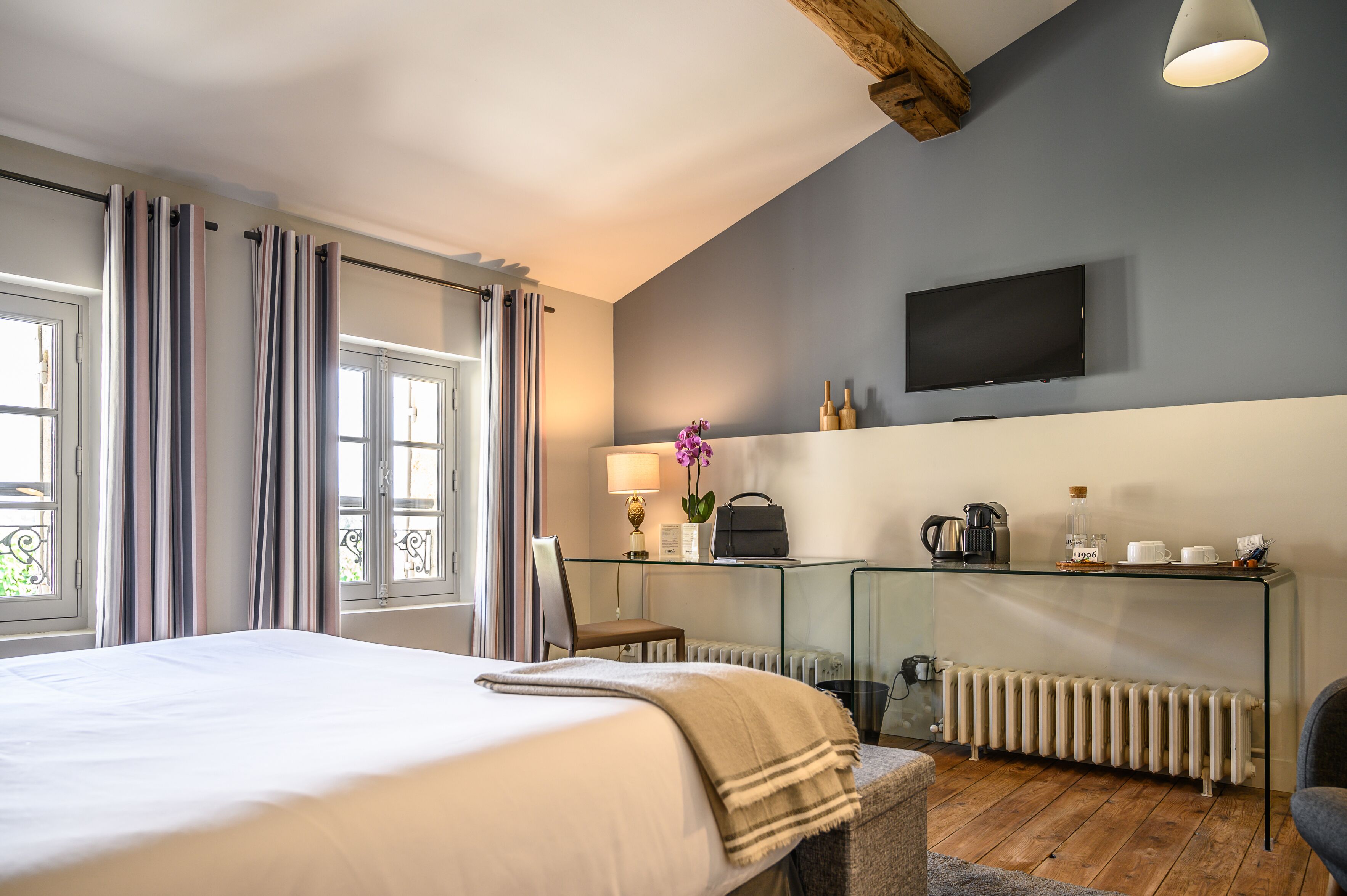 Een hotelkamer met een bed, een glazen bureau met lamp, een televisie en een radiator.