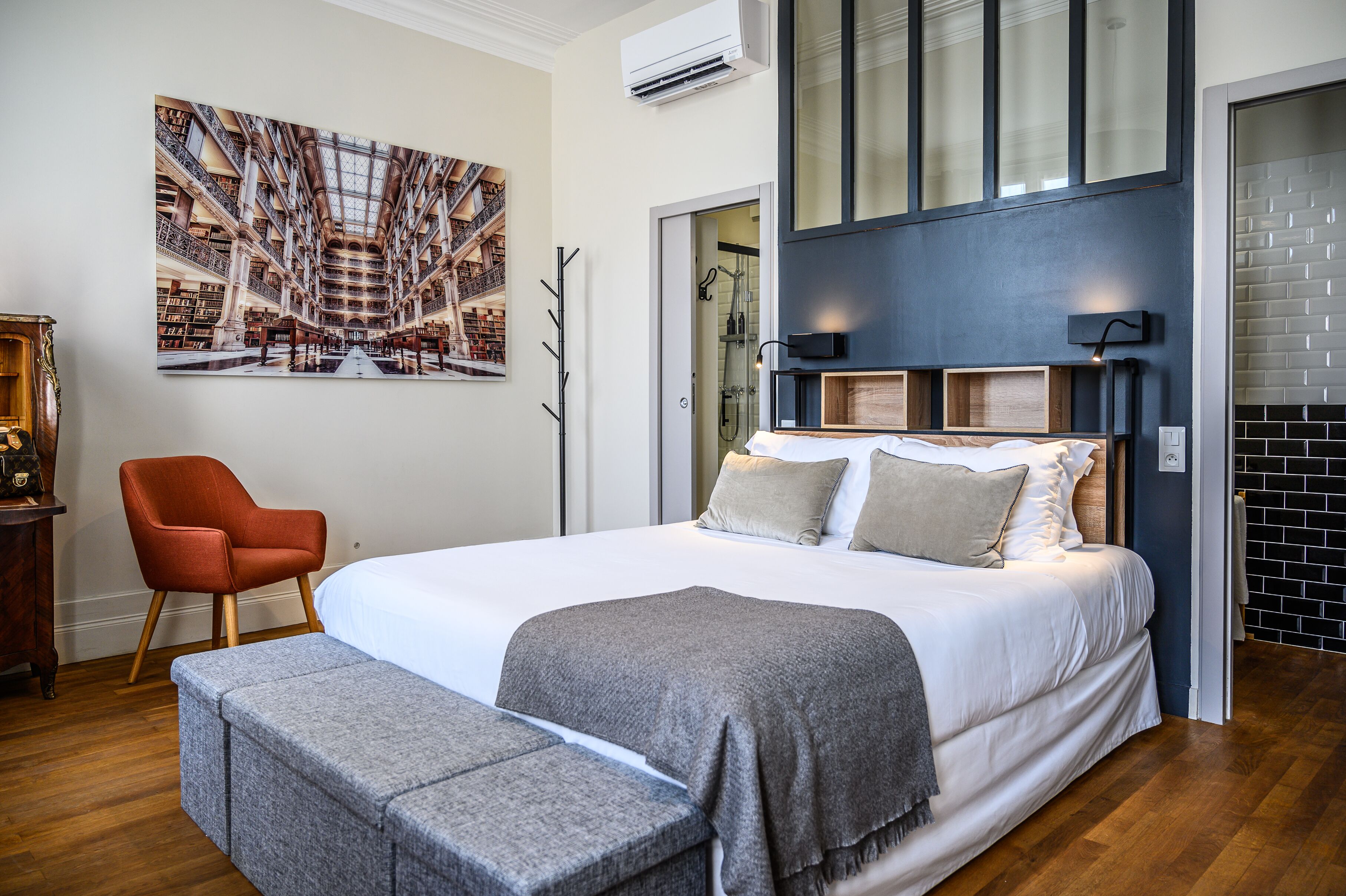 A bedroom with a large bed, a chair, a bench, a painting, and a fireplace.