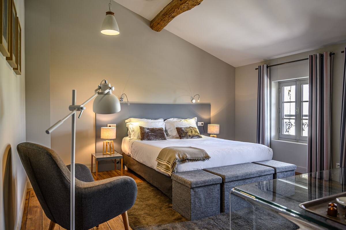 Ein modernes Schlafzimmer mit einem großen Bett, Nachttischlampen, einer Bank und Blick ins Freie.