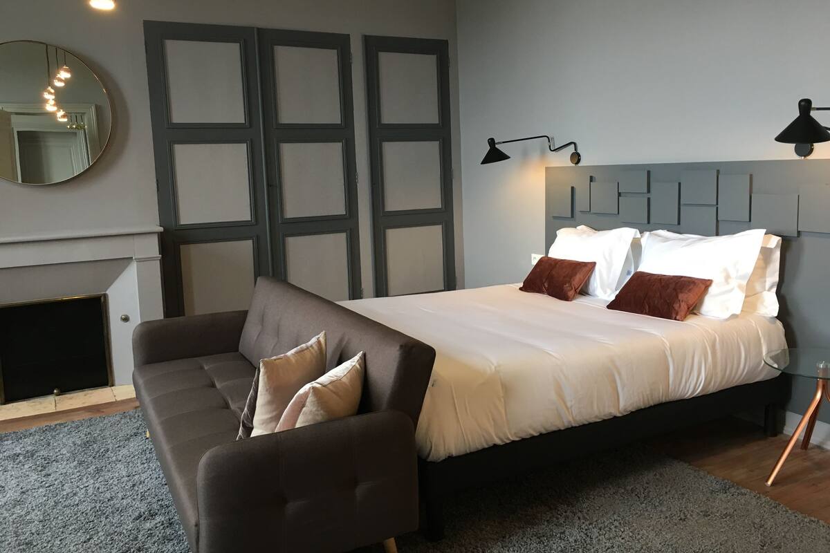 Ein Schlafzimmer mit Bett, Sofa, Spiegel und Kamin.