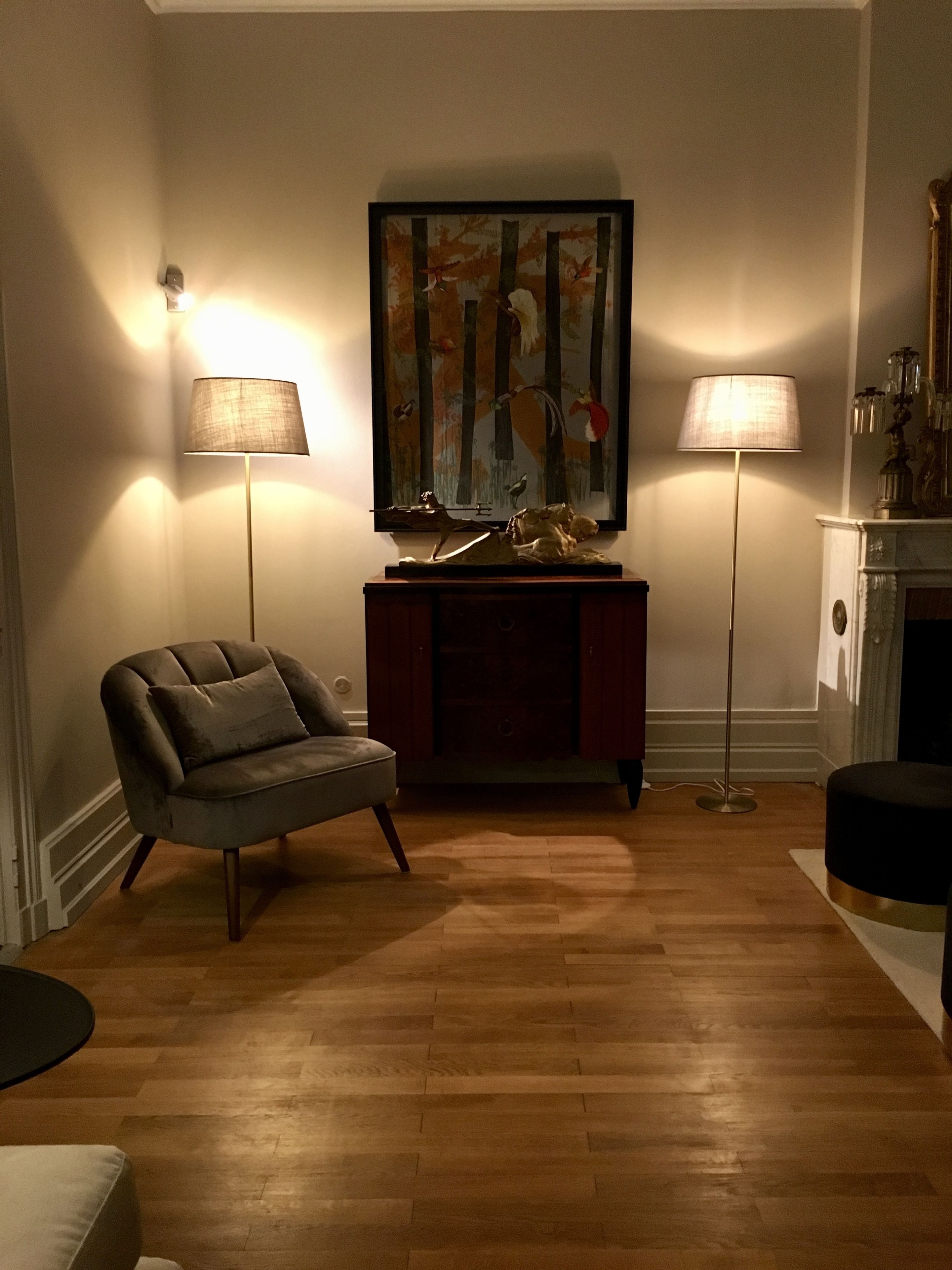 Una sala de estar con sofá, una mesita auxiliar, un cuadro y dos lámparas de pie.