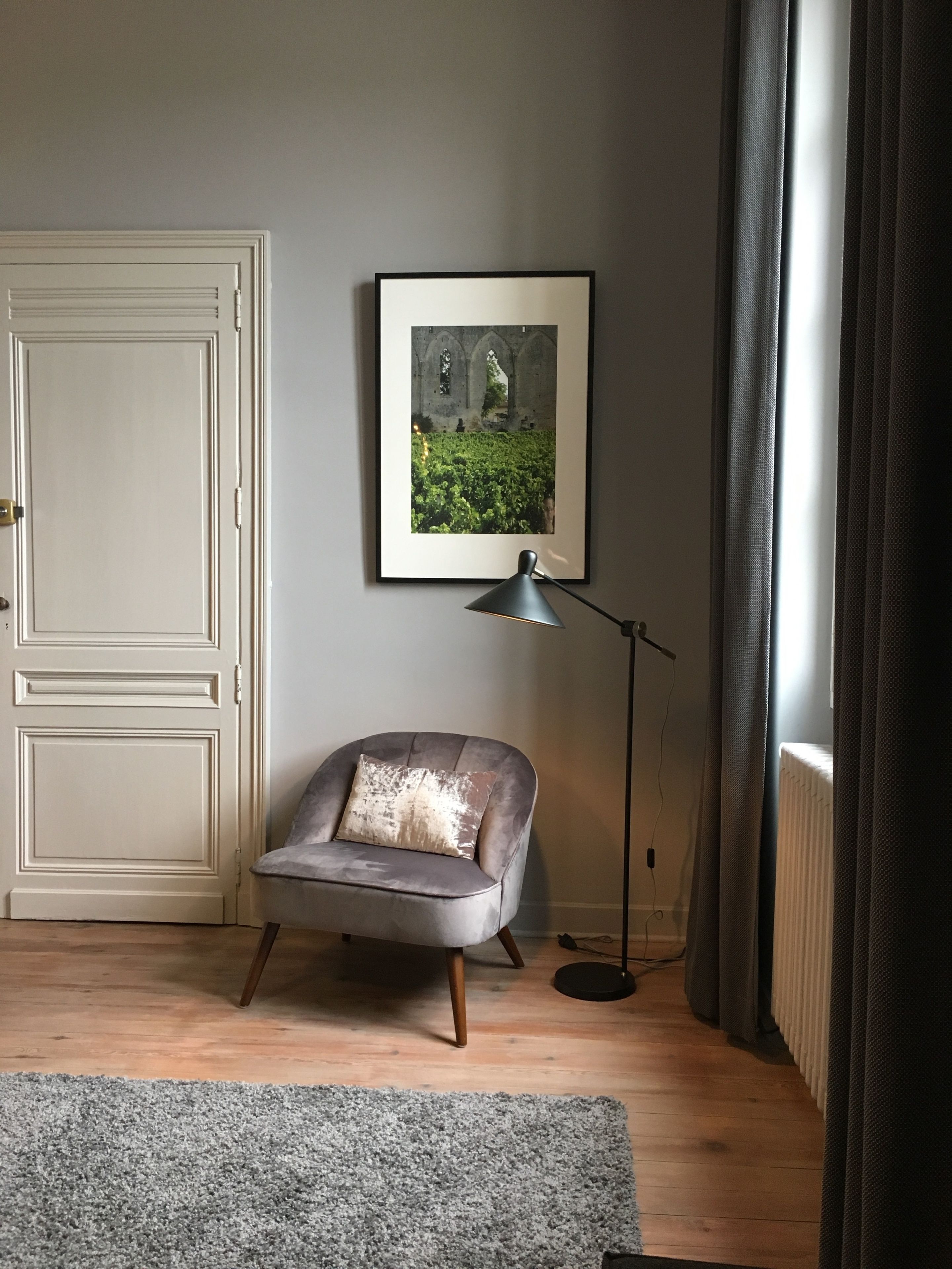 A room with a grey armchair, a framed picture on the wall, a floor lamp, and a closed door.