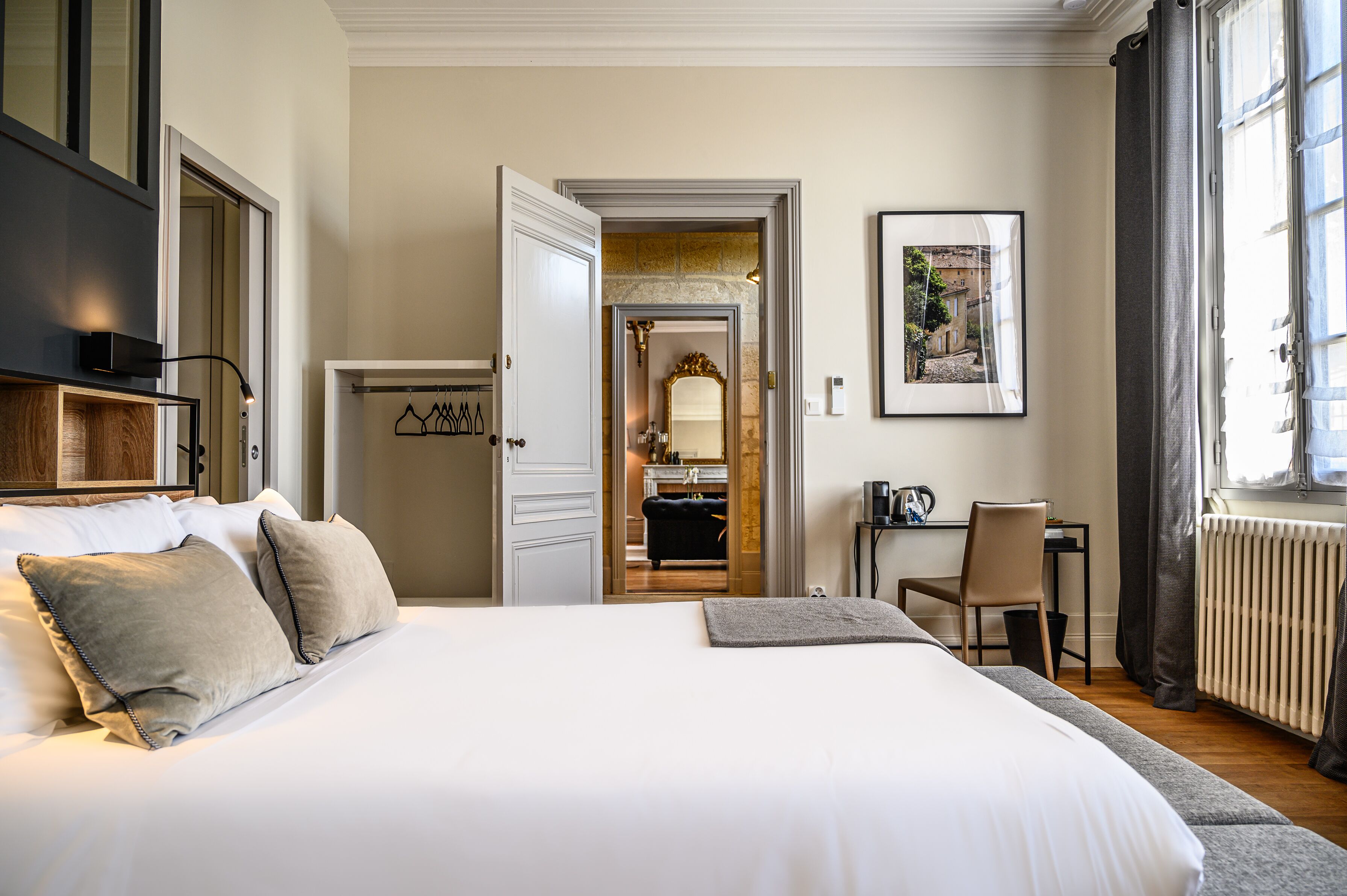 A hotel room with a large bed, a desk, and a view of the city through the open door.