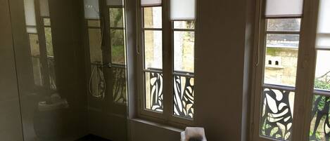 A bathroom with a shower, a toilet, and a window with a decorative screen.