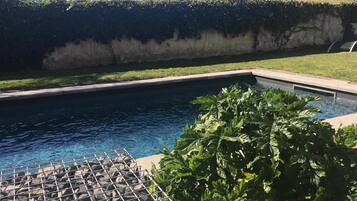 A swimming pool with a metal grill in the foreground, surrounded by a hedge and a grassy area.