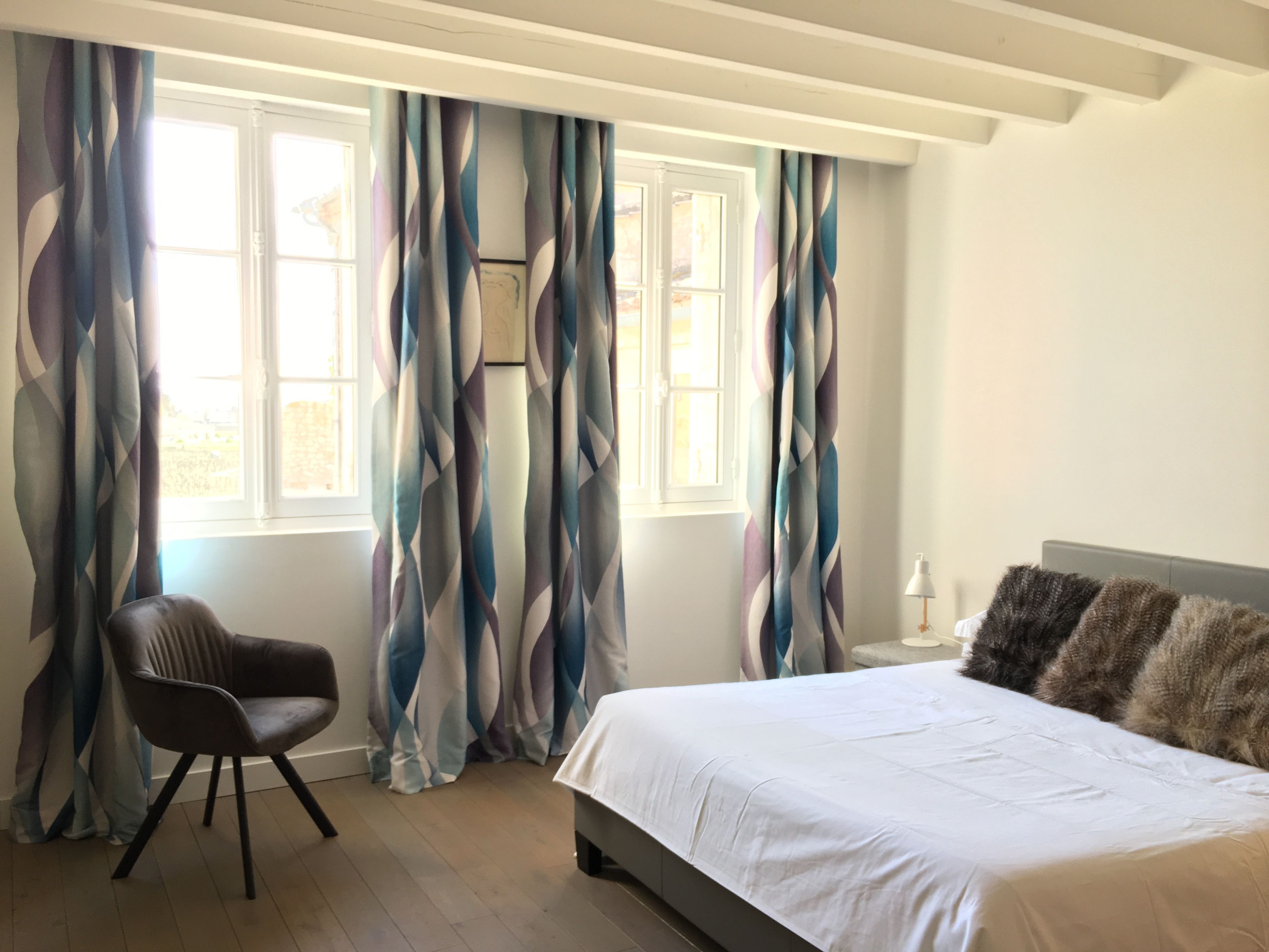 Un dormitorio con cama, una silla y cortinas.