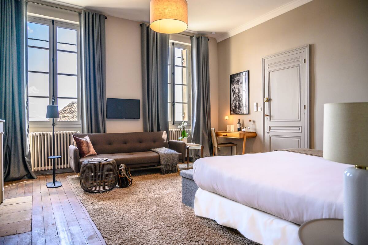 Ein Hotelzimmer mit einem großen Bett, einem Schlafsofa, einem kleinen Tisch, einer Lampe, einer Heizung und einem Fernseher an der Wand.