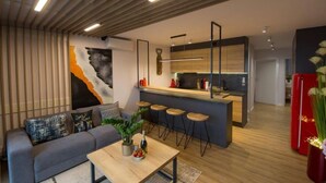 Una sala de estar moderna con un sofá gris, una mesa de centro de madera y una cocina con barra y taburetes.