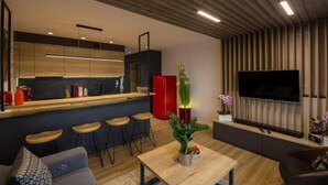 Una sala de estar moderna con techo de madera, una zona de cocina con refrigerador rojo y un televisor de pantalla plana montado en la pared.