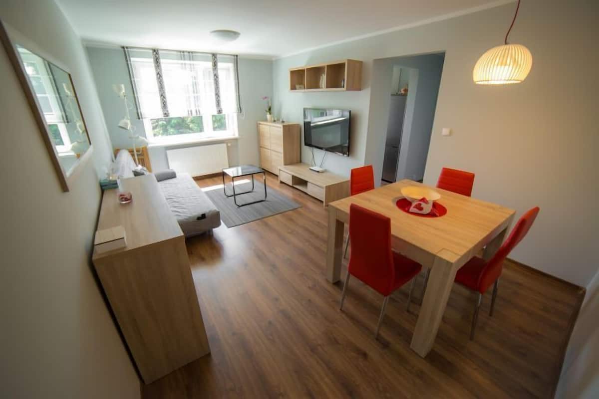 Un salon moderne avec une table à manger en bois, des chaises rouges, un téléviseur et un canapé.