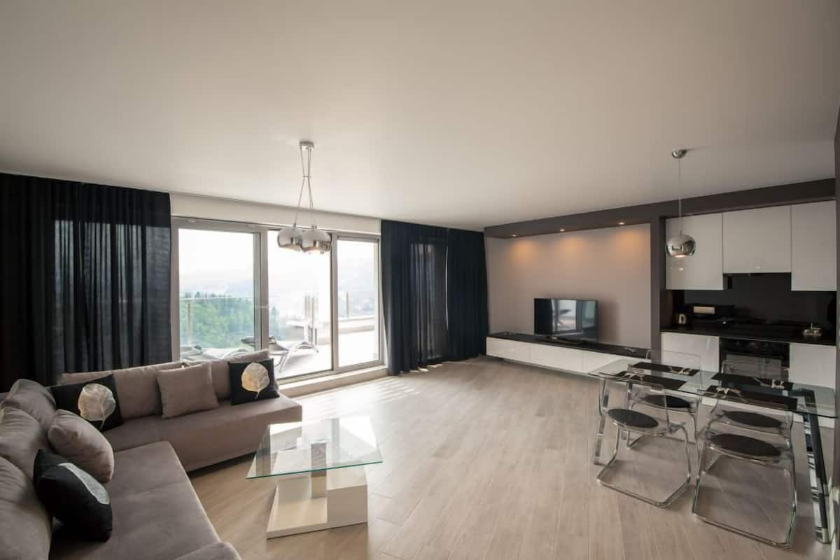 Un salon moderne avec une table basse en verre, un canapé avec des coussins et un coin repas comprenant une table et des chaises en verre.
