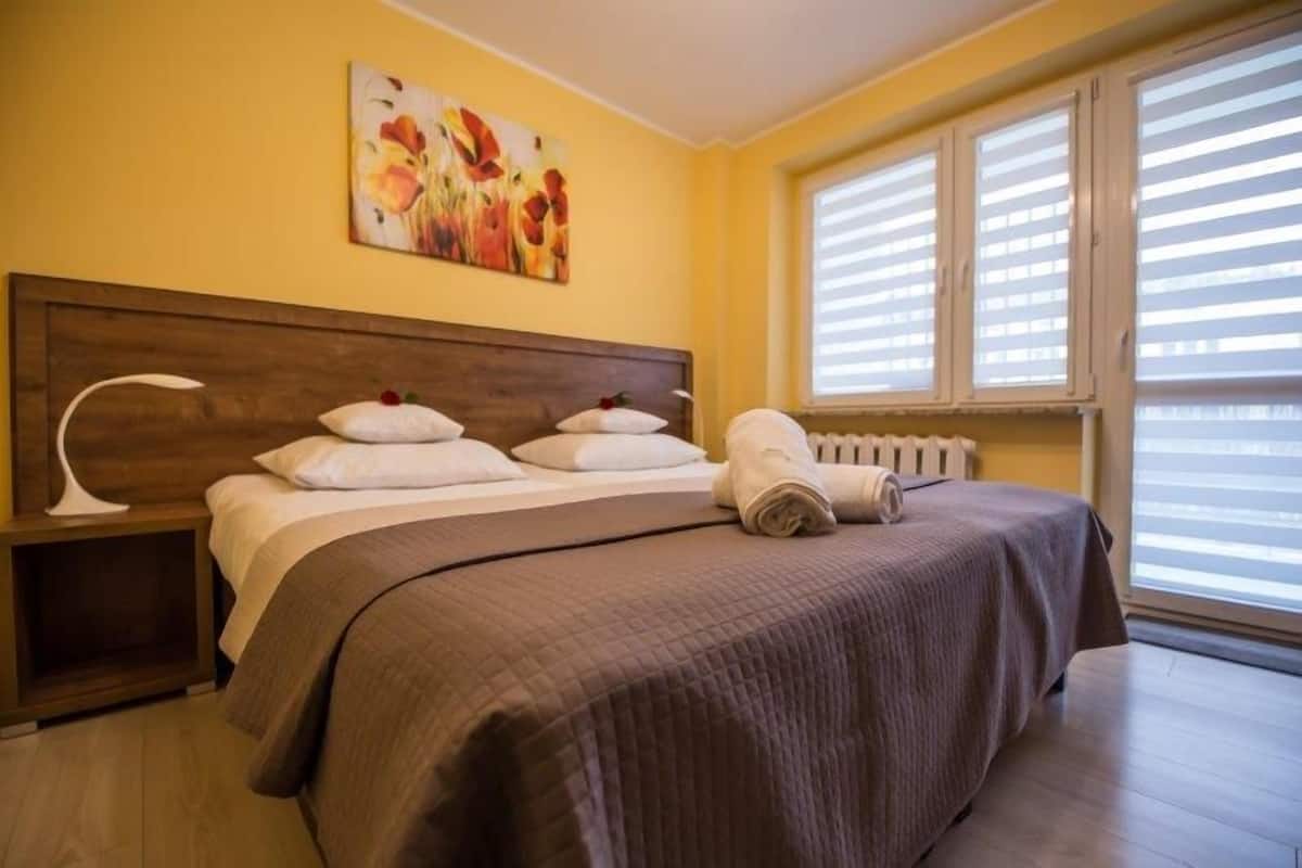 Une chambre d’hôtel avec un grand lit, une table de chevet, un radiateur et une fenêtre avec des stores.