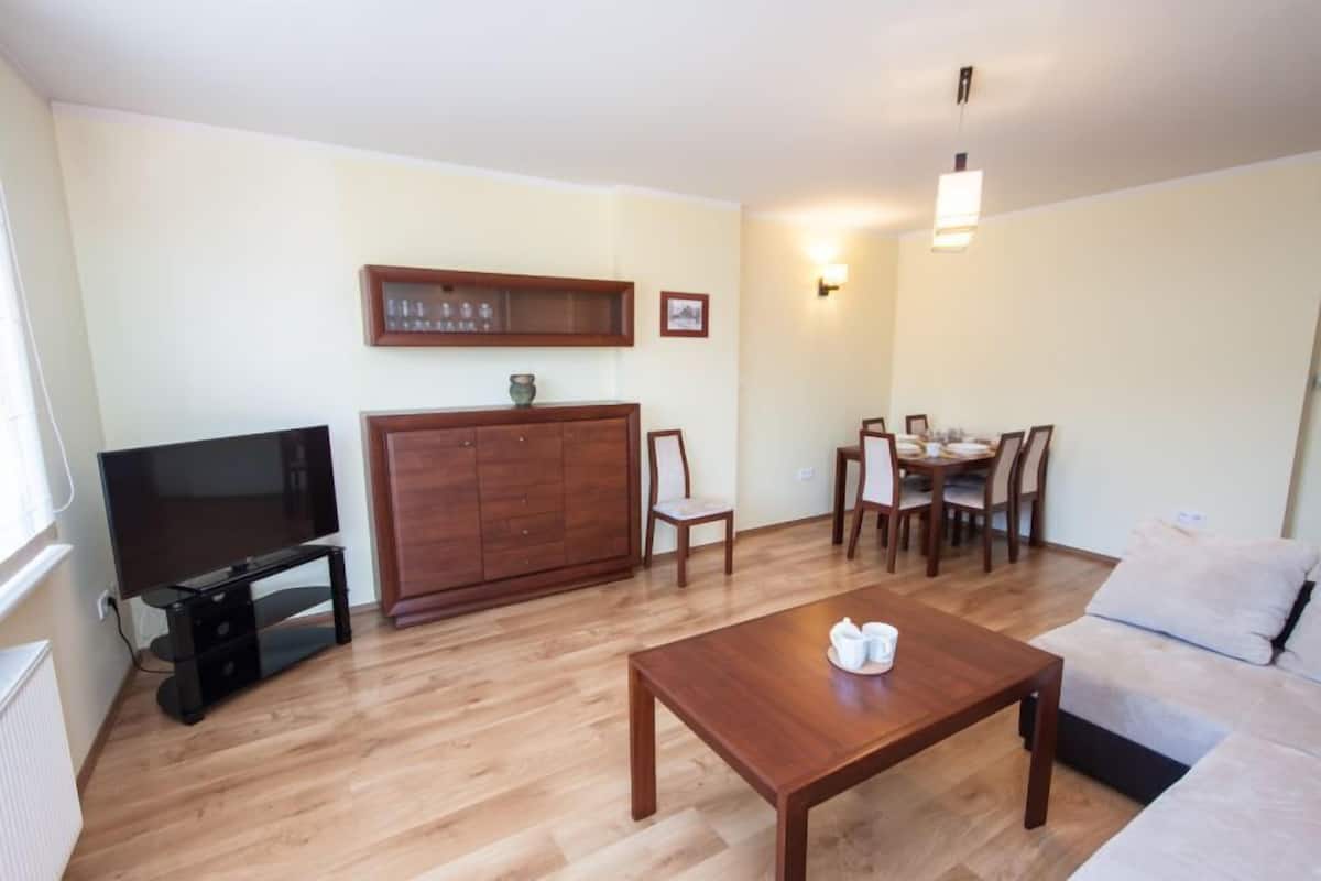 Un salon comprenant un téléviseur, un meuble en bois, une table à manger, des chaises et un canapé.