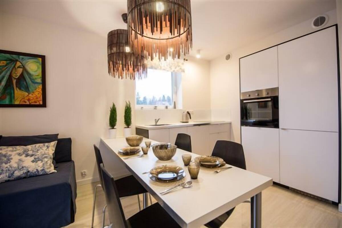 Une cuisine moderne avec des meubles blancs, une table à manger dressée avec des bols et des assiettes, et un luminaire suspendu.