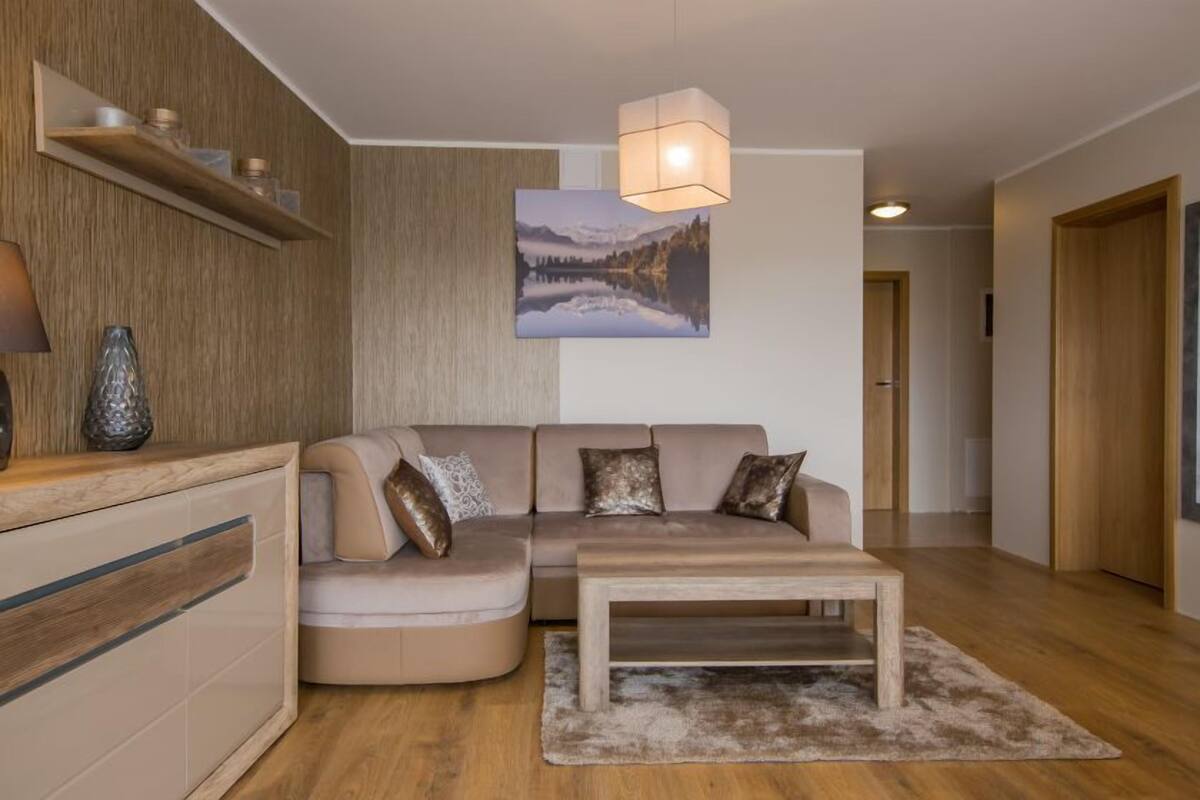 Un salon moderne avec un canapé d’angle beige, une table basse en bois et un tableau représentant un paysage de montagne.